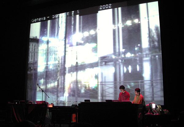 Two performers beneath a large projection of layered internet imagery at the Museum of Contemporary Art Chicago